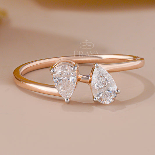 Rose gold ring with two pear-shaped diamonds on a beige background, featuring the brand 'Eraya'.