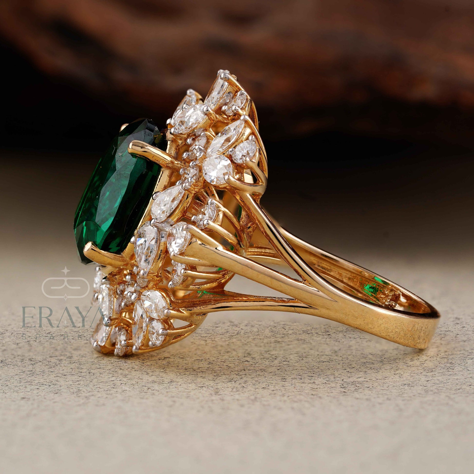 Gold ring with emerald and diamonds on a textured surface, featuring the brand 'Eraya'.