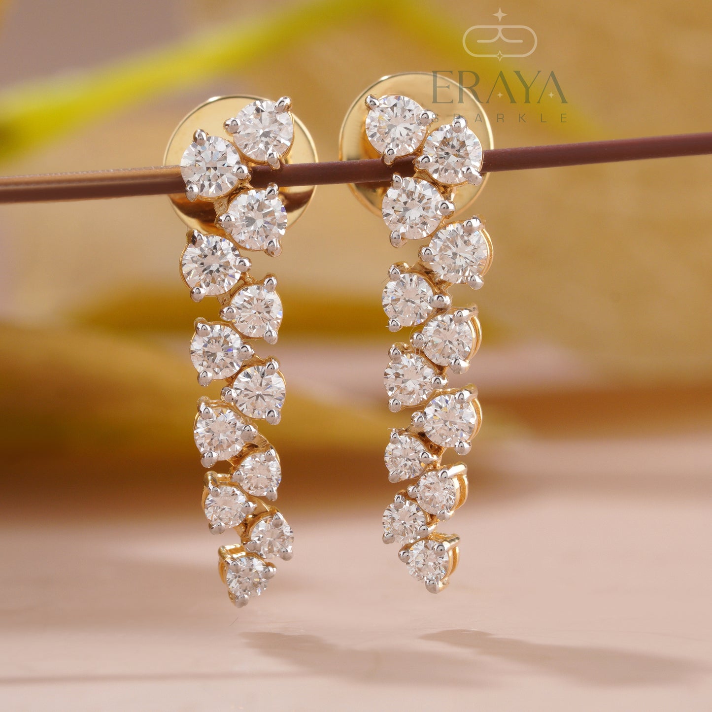 Gold earrings with clear gemstones on a blurred background, featuring the brand 'Eraya'.