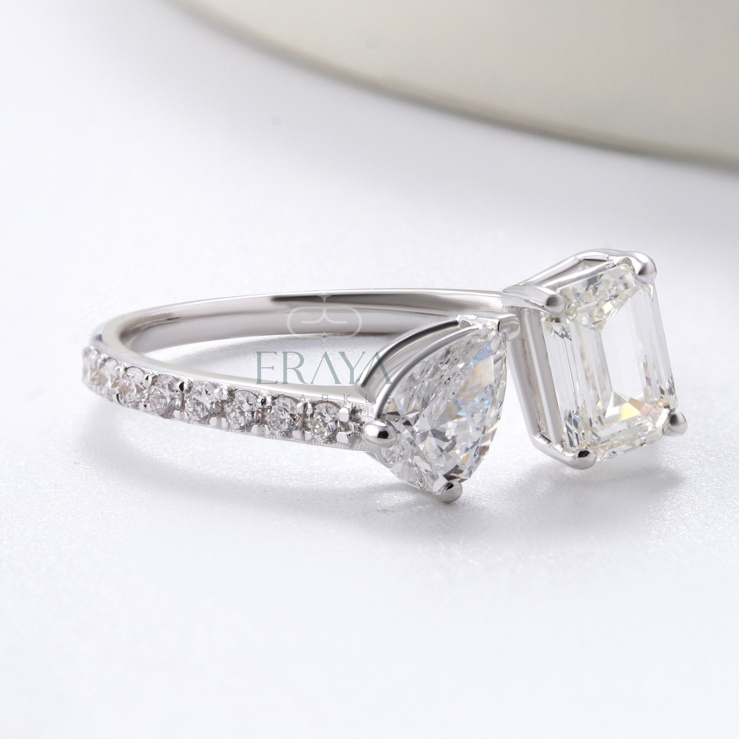 Silver ring with a large diamond and smaller diamonds on the band, on a light background.