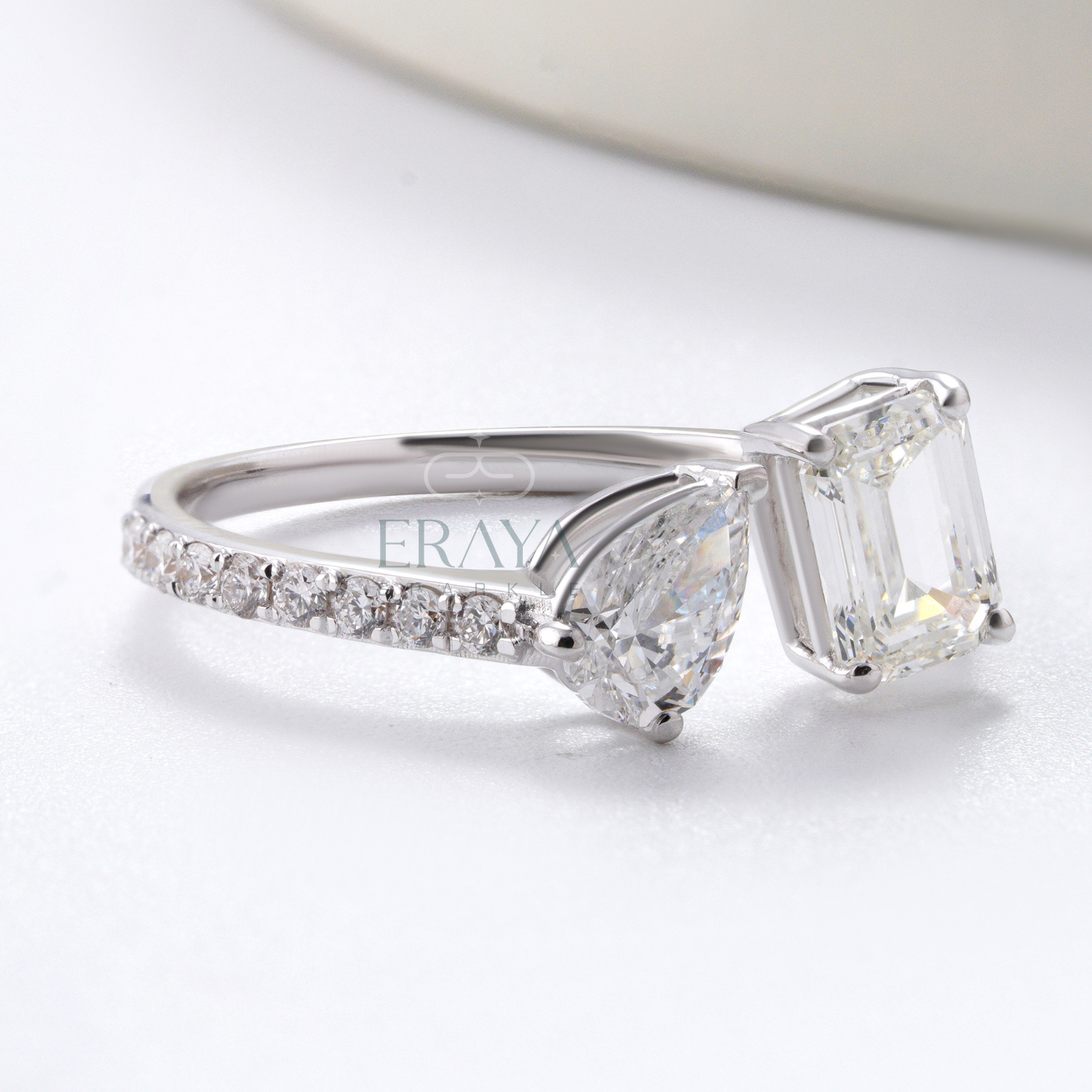 Silver ring with a large diamond and smaller diamonds on the band, on a light background.