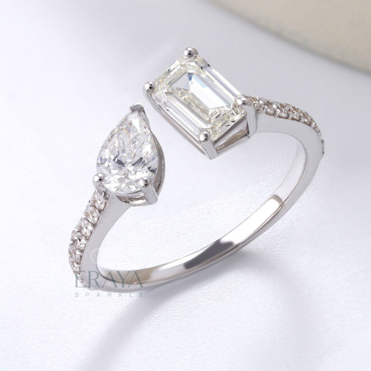 Diamond ring with pear-shaped and emerald-cut diamonds on a light background